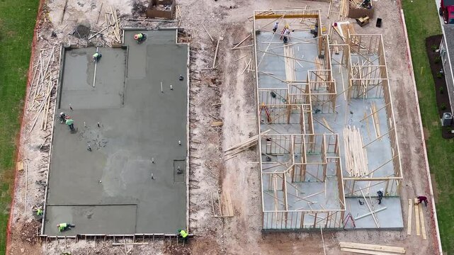 Aerial view of newly poured concrete slab next to home that is being constructed with wooden framework in Georgetown Texas