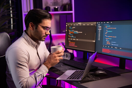 Smart IT developer drinking coffee cup while working in software development coding on pc screen, presenting program application update online website database at neon lighting cyber office. Surmise.