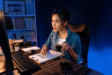 Thinking young beautiful Asian creative woman looking on pc with holding coffee cup, pointing sales target report on business market graph folder paperwork report at neon at night time. Stratagem.