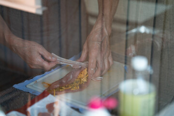 A person skillfully rolls sliced meat with cheese and noodles on a countertop, showcasing culinary expertise in a sunlit kitchen setting during the day.