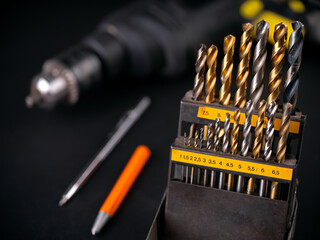 Drill bits in a box against the background of a drill and center punch. Dark background.