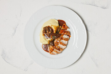 Mashed potatoes with sliced ​​steak and sauce in a white plate