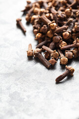 A close-up of dried cloves scattered on a textured gray surface asian Indian Indonesian spice. Warming spices in cookery. Vertical shoot with space for text.