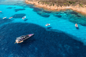 Aerial view of luxury yachts and boats on blue sea, beautiful island on summer sunny day. Sandy beach, rocky sea coast, turquoise transparent water in Sardinia, Italy. Top drone view. Seascape