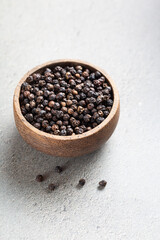 Indian spice black pepper in wooden bowl on gray background with space for text. Indian Ayurvedic spice. Flavor enhancer. Vertical shoot.
