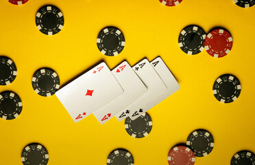 Four aces are displayed on a bright yellow surface surrounded by an array of black and red poker...