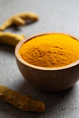 Turmeric powder in wooden bowl and dried turmeric roots on grey background close-up. Herbal alternative Ayurvedic medicine. Indian spices. Antibacterial food.