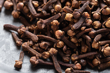 A close-up of dried cloves scattered on a textured gray surface Indian Indonesian spice. Herbal alternative Ayurvedic medicine. 
