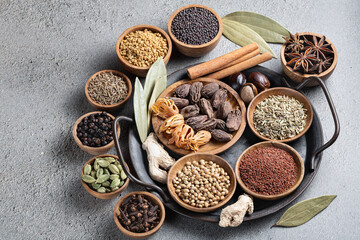 A variety of whole colorful Indian spices in wooden bowls on a gray top view. Ayurvedic spices. Seasoning for healthy food. 