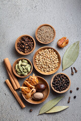 A variety of whole colorful Indian spices in wooden bowls on a gray background directly above vertical shoot. Ayurvedic spices. Healthy food. 