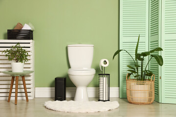 Ceramic toilet bowl, houseplants and necessities near green wall indoors