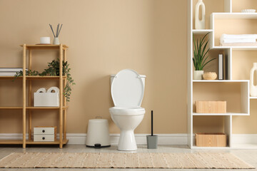 Toilet bowl, brush and necessities near beige wall in restroom