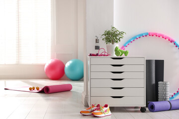 Different fitness equipment, sneakers and chest of drawers indoors