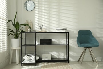 Console table with different decor and chair near white wall indoors. Interior design