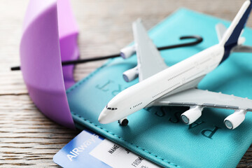 Travel insurance. Plane model, passport, small umbrella and ticket on wooden table, closeup