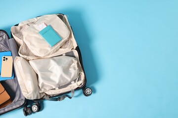 Suitcase with clothes, smartphone and other belongings on light blue background, top view. Space...