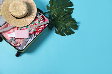 Open suitcase with different clothes, hat and passport on light blue background, flat lay. Space...