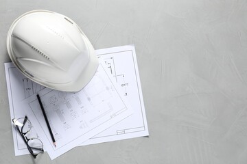 Different engineering drawings, hard hat, pencil and glasses on grey table, flat lay. Space for text