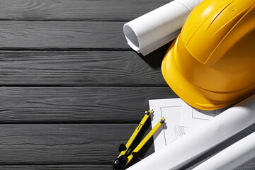 Different engineering drawings, hard hat and divider on grey wooden table, above view. Space for...