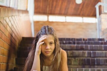Teenage girl sitting on brick steps in covered stairwell, leaning head on hand with metal handrail