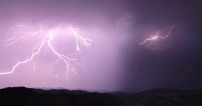 Lightning storm in the night sky at mountain. Multiple lightnings and thunders illuminate night sky and hills