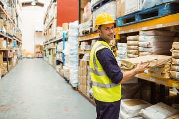 Male warehouse worker retrieving cardboard box from orange and blue racks in warehouse, copy space