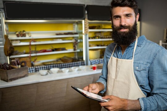 Man standing behind deli counter with tablet and hanging cured meats on shelves, copy space