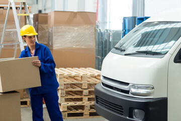 Young woman lifting cardboard box at loading dock, stacking pallets by delivery van and ladder © wavebreak3