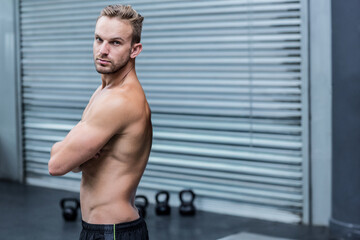 Fototapeta premium Man standing with crossed arms in fitness studio, showing kettlebells, copy space