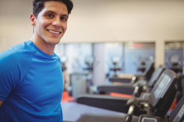 Man standing by row of treadmills and ellipticals in bright gym, smiling at camera, copy space