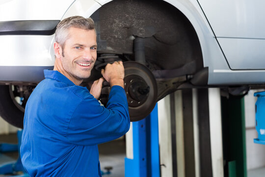 Male mechanic servicing brake rotor and suspension on lifted silver car in garage, copy space