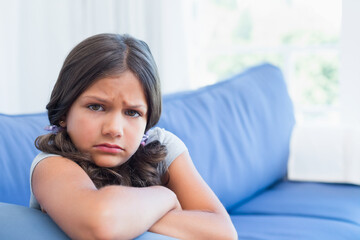 Young girl leaning on blue sofa in living room, pouting expression under natural light, copy space