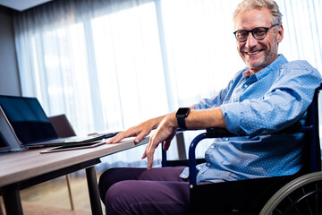 Man working at desk in office from wheelchair, using laptop smartphone and smartwatch, copy space