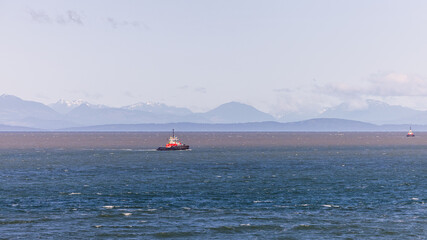 Obraz premium Red Tugboat in Coastal Waters with Mountains in the Background