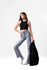 Model posing in casual outfit with black top and denim jeans in a minimalist studio setting during...
