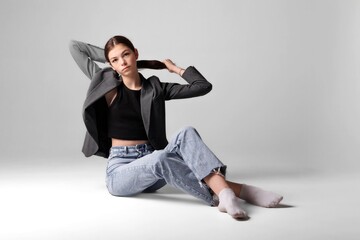 Young woman in casual attire poses in a studio setting with a minimalist background for a fashion photoshoot