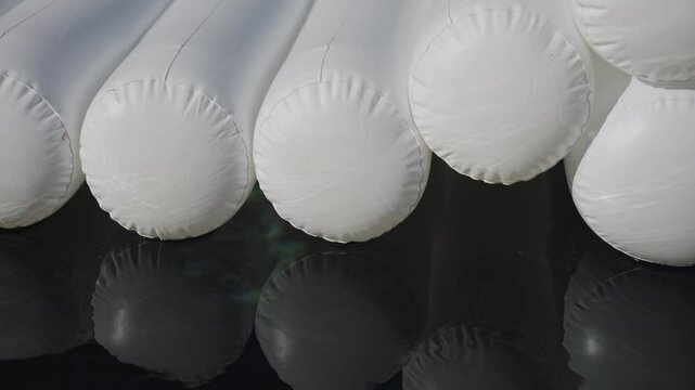 A row of white inflatable pool floats are lined up on a dark surface. The floats are all the same size and shape, and they are all white. The image has a calm and peaceful mood