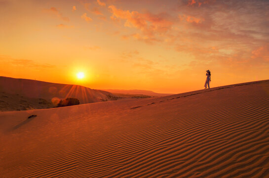 Side view of a Woman in a traditional Ao Dai dress and non la hat walking in the Mui Ne Sand Dunes at sunset, Mui Ne, Phan Thiet, Vietnam