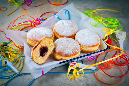 Authentic traditional German festive Berliner Krapfen - jam doughnut with icing sugar as close-up in a rustic tray with carnival party decoration
