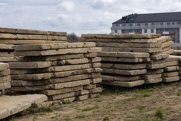 Stacks of old weathered concrete slabs at construction site with modern residential building in...