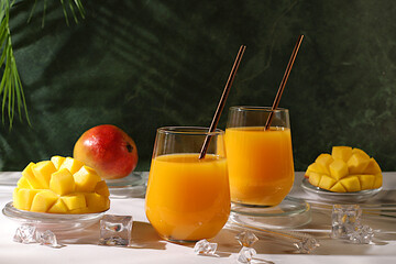 Cold homemade lemonade cocktail, juice or smoothie with mango, ice and fruits on dark table,...