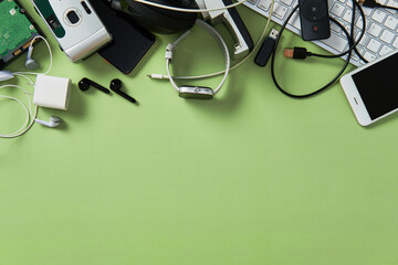 Old electronic devices and gadgets like phones, keyboards, headphones on green background. E-waste...