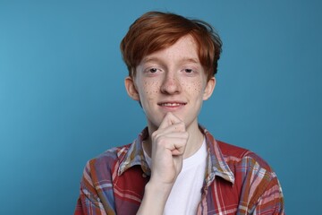 Smiling teenage boy with freckles on light blue background