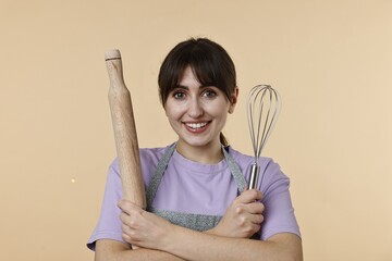 Woman with rolling pin and whisk on beige background