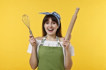 Excited woman with rolling pin and whisk on yellow background