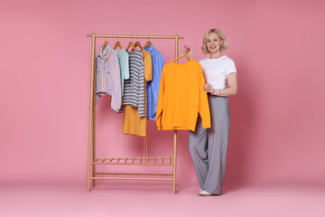 Smiling fashion stylist and rack with clothes on pink background