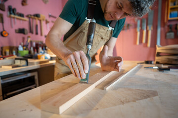 Professional carpenter concentrates on perfecting wood surface with chisel, eliminating tiny...
