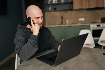 Freelancer working from remote home office, talking on mobile phone and using laptop computer,...