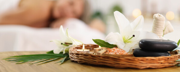 Senior woman relaxing on massage couch indoors, selective focus. Different spa products and lily flowers on table