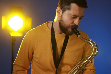 Professional musician playing saxophone on blue background with light